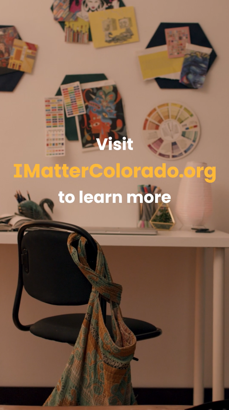 A desk with art supplies, a colorful handbag hanging on a black chair, and a wall decorated with various colorful art projects and a color wheel.