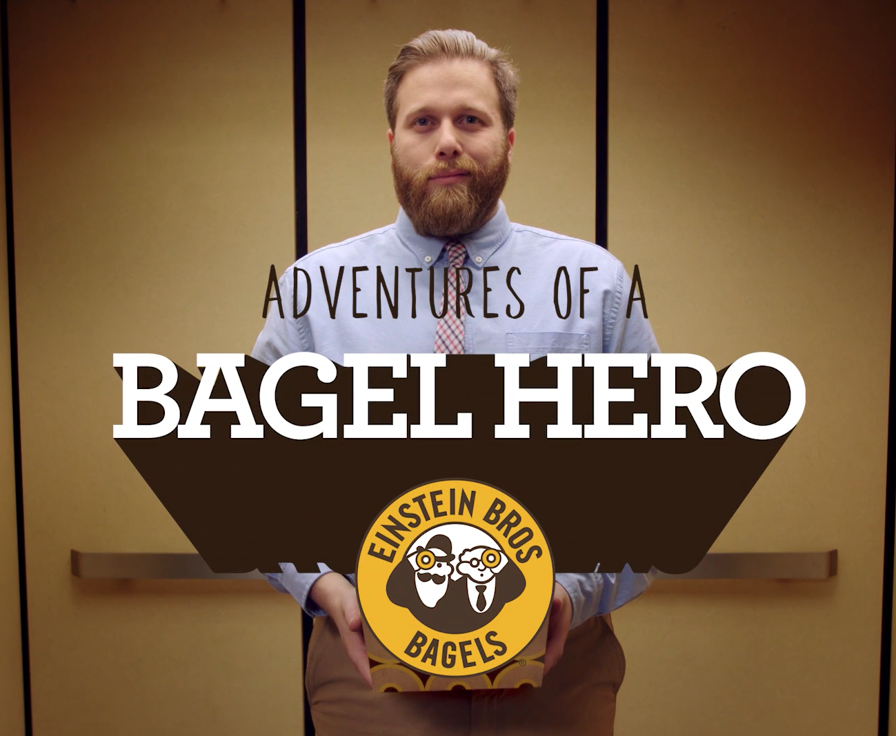 A man with a beard in a light blue shirt holding a box of bagels. The text overlay reads 'Adventures of a Bagel Hero' with a logo at the bottom displaying two characters and the text 'Einstein Bros Bagels'.