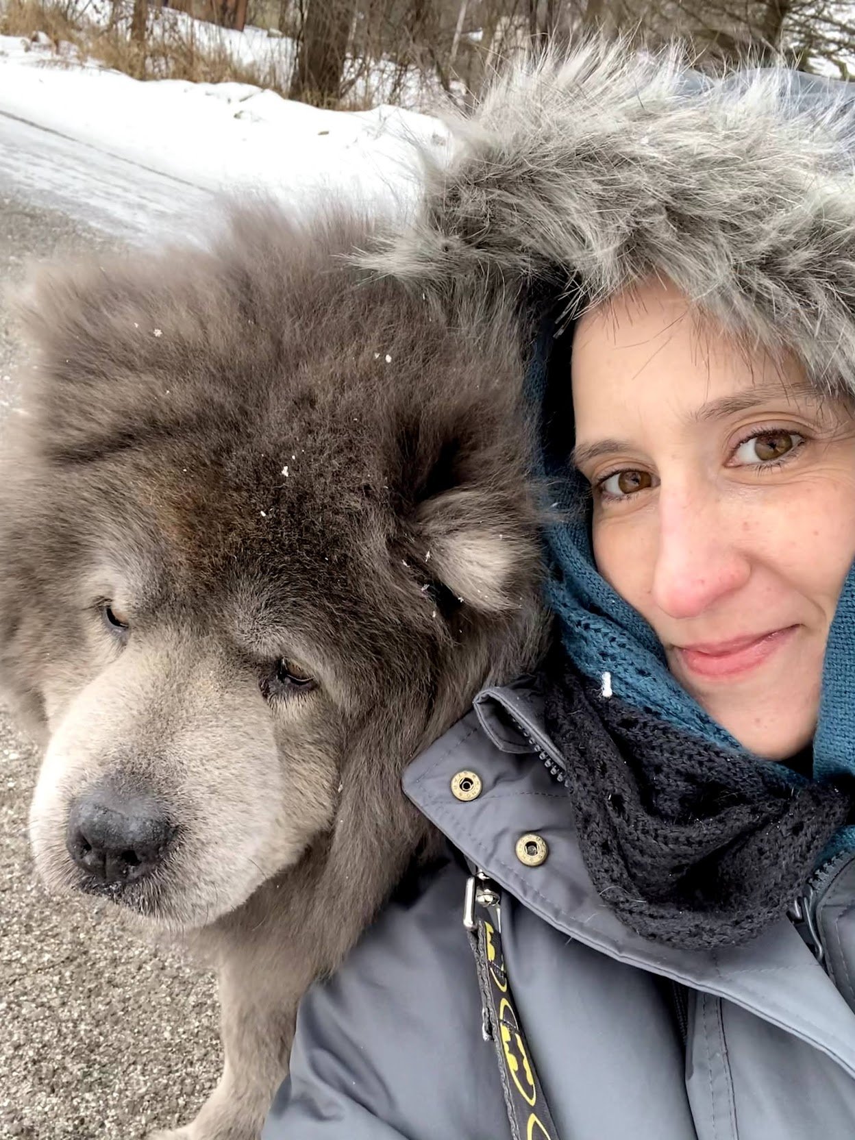 A woman in winter clothing taking a selfie with a large husky dog outdoors in winter.