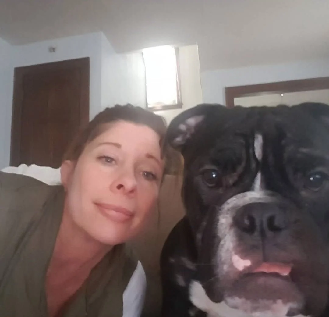 A woman and a large black and white dog lie close together on a bed in a bedroom with a wooden door and a window.