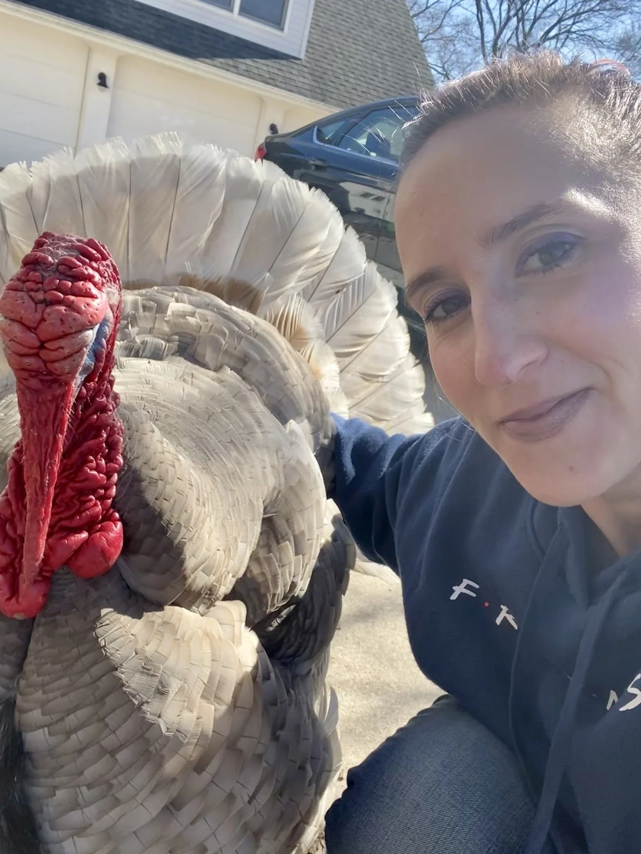 A woman taking a selfie with a large turkey made of woven materials outdoors on a sunny day.