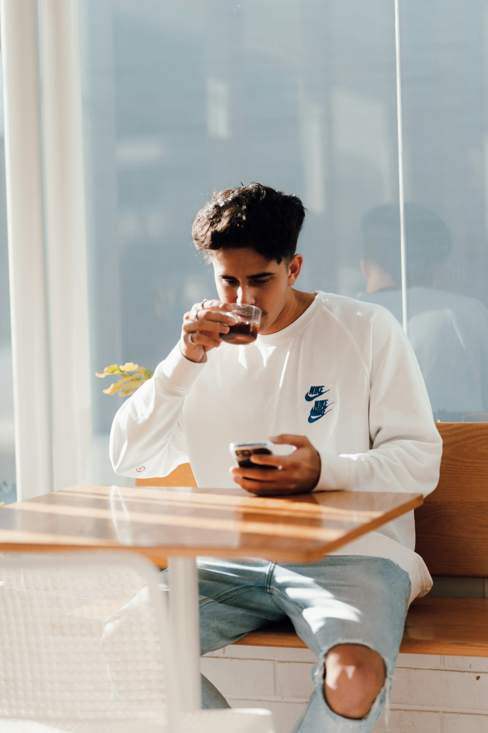 Young man sitting alone at a café table with coffee and phone, reflecting quietly — symbolizing individual therapy for adults and young adults in Chicago.
