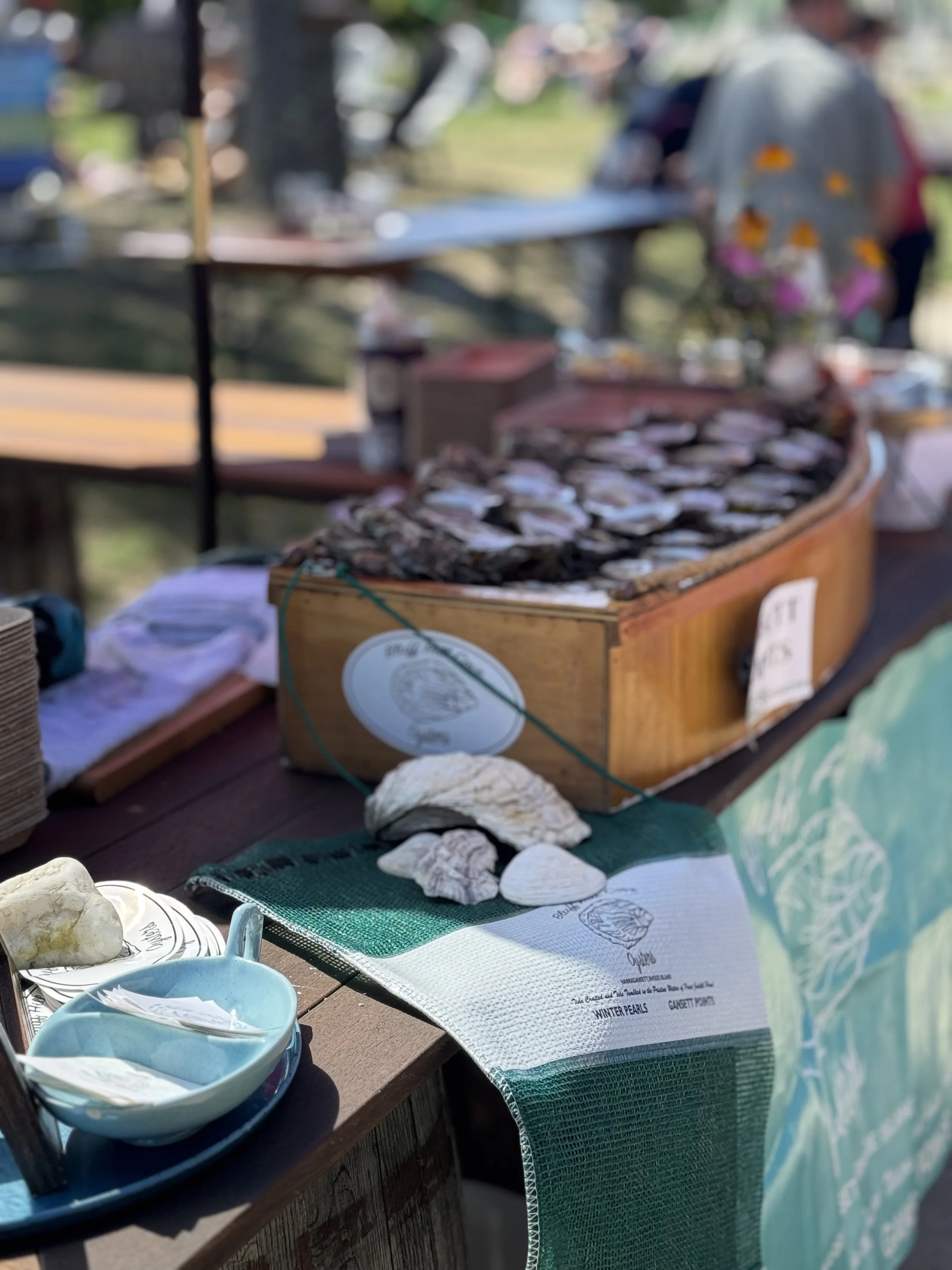Display of assorted shells, a piece of coral, and a ceramic dish on a table at a seafood market or outdoor vendor stand.