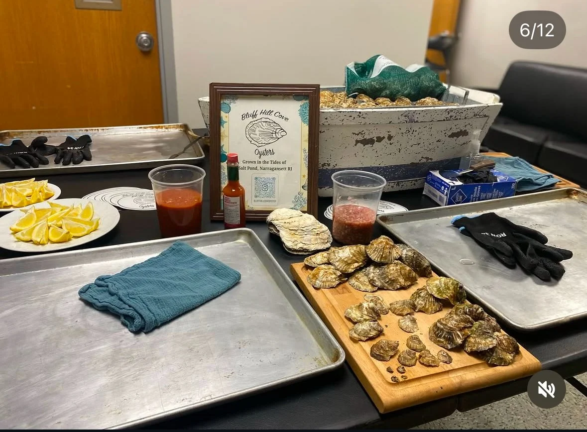 Table with oyster display, lemon wedges, hot sauce, and oyster knife, with a framed sign about oysters at Bluff Hill Cove, Rhode Island.