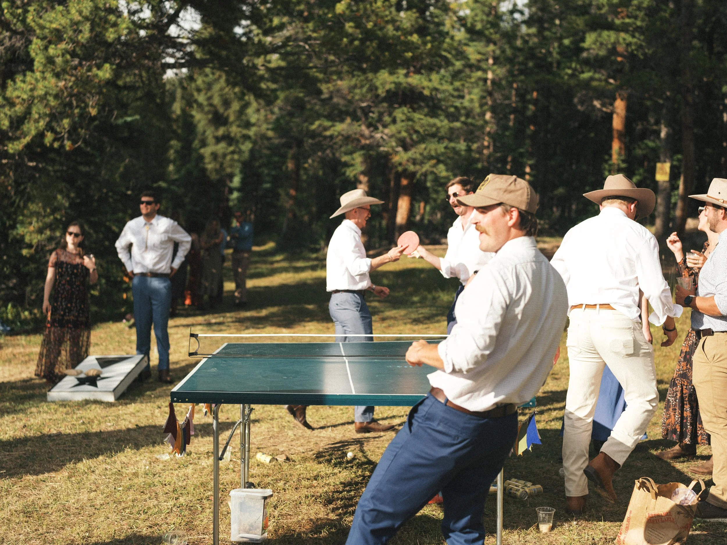 People playing table tennis outdoors in a park with trees in the background.