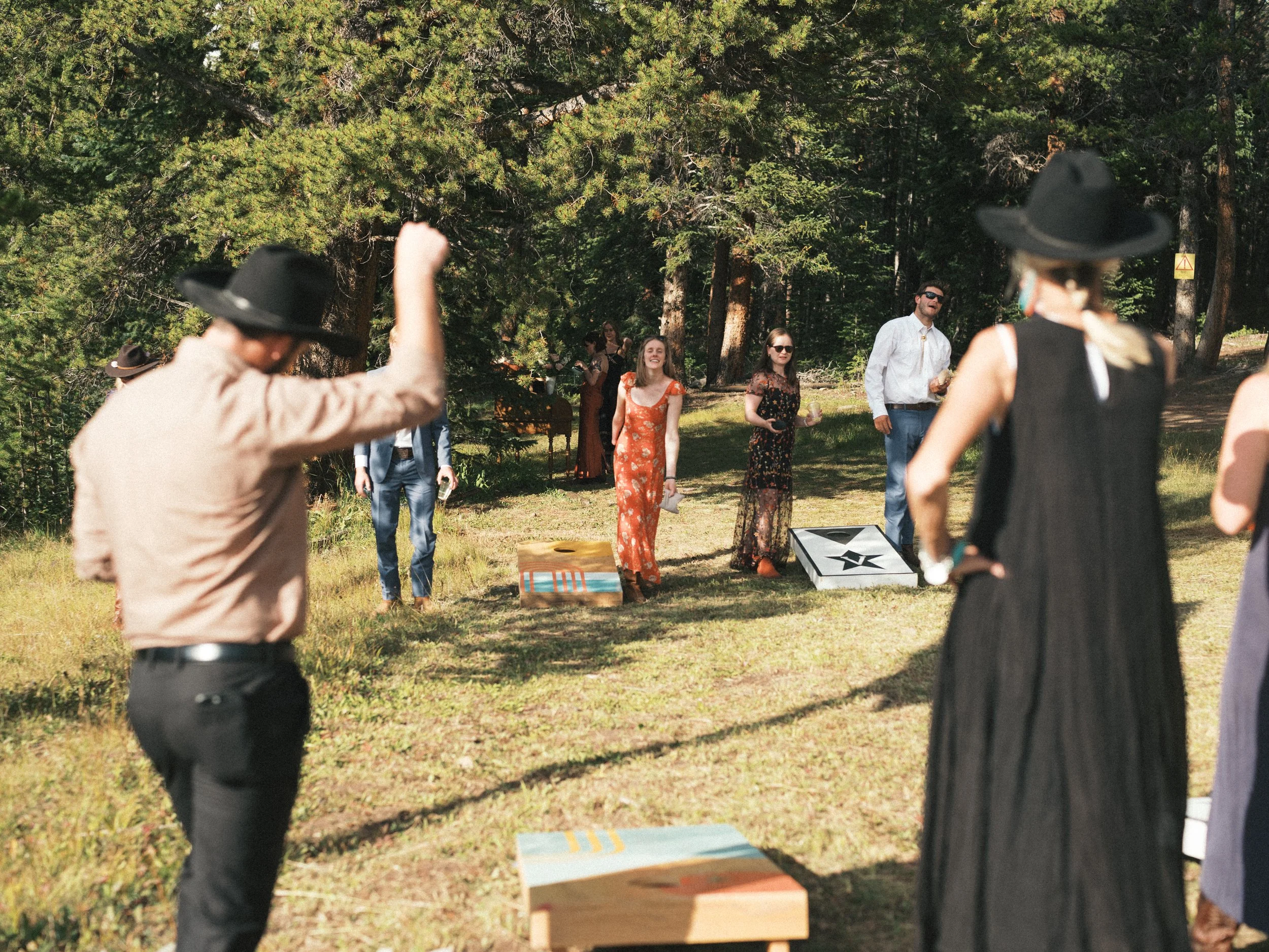 People playing a game of cornhole in a wooded outdoor setting during daytime.