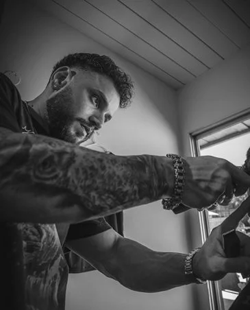 A man with tattoos and a beard looking out the window while adjusting or handling something with his hands.
