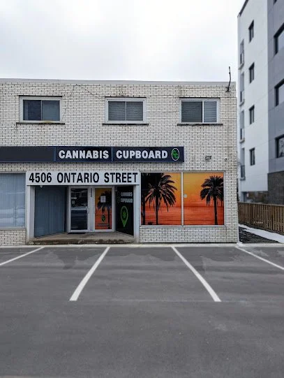 storefront with a sign that reads Cannabis Cupboard above the entrance, located at 4506 Ontario Street, with a parking lot in front and a painted mural of palm trees on the window.