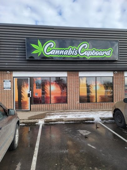 The storefront of Cannabis Cupboard, a retail store, with windows displaying sunset scenes and a sign with a green cannabis leaf logo.