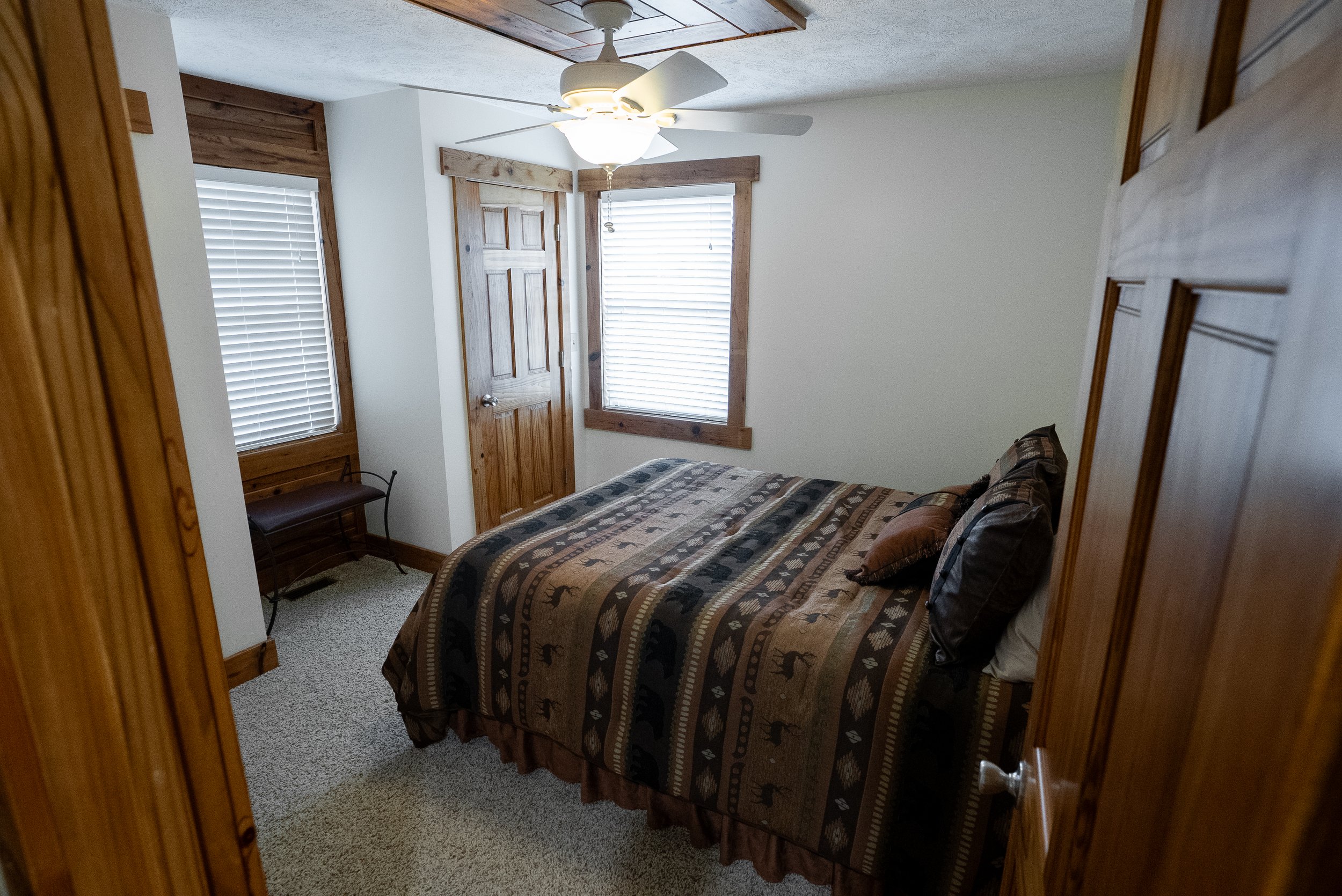 A small bedroom with a bed, wooden trim, and a ceiling fan with lights.
