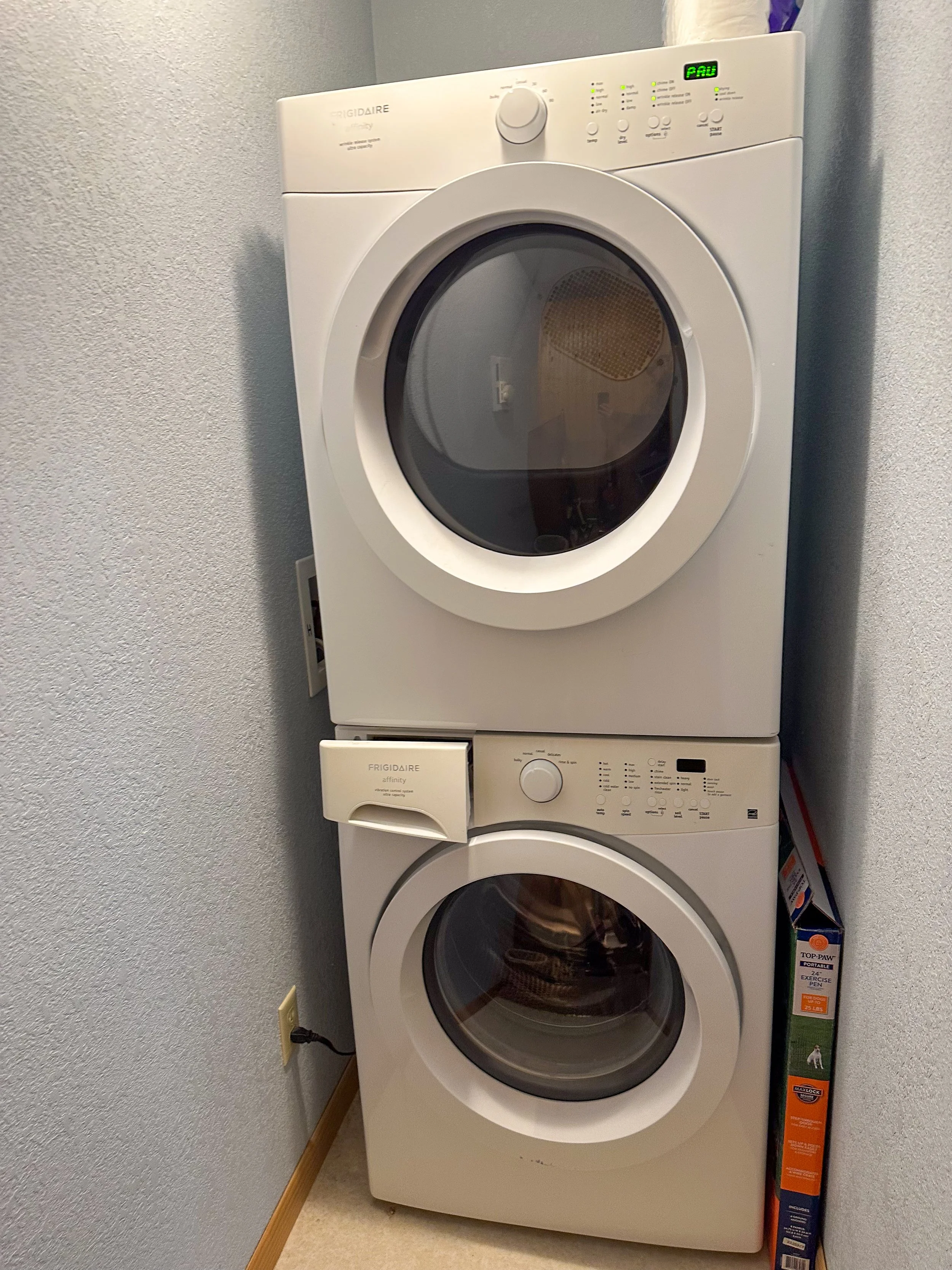 Stacked white Frigidaire front-loading washing machine and dryer in a laundry room with gray walls.