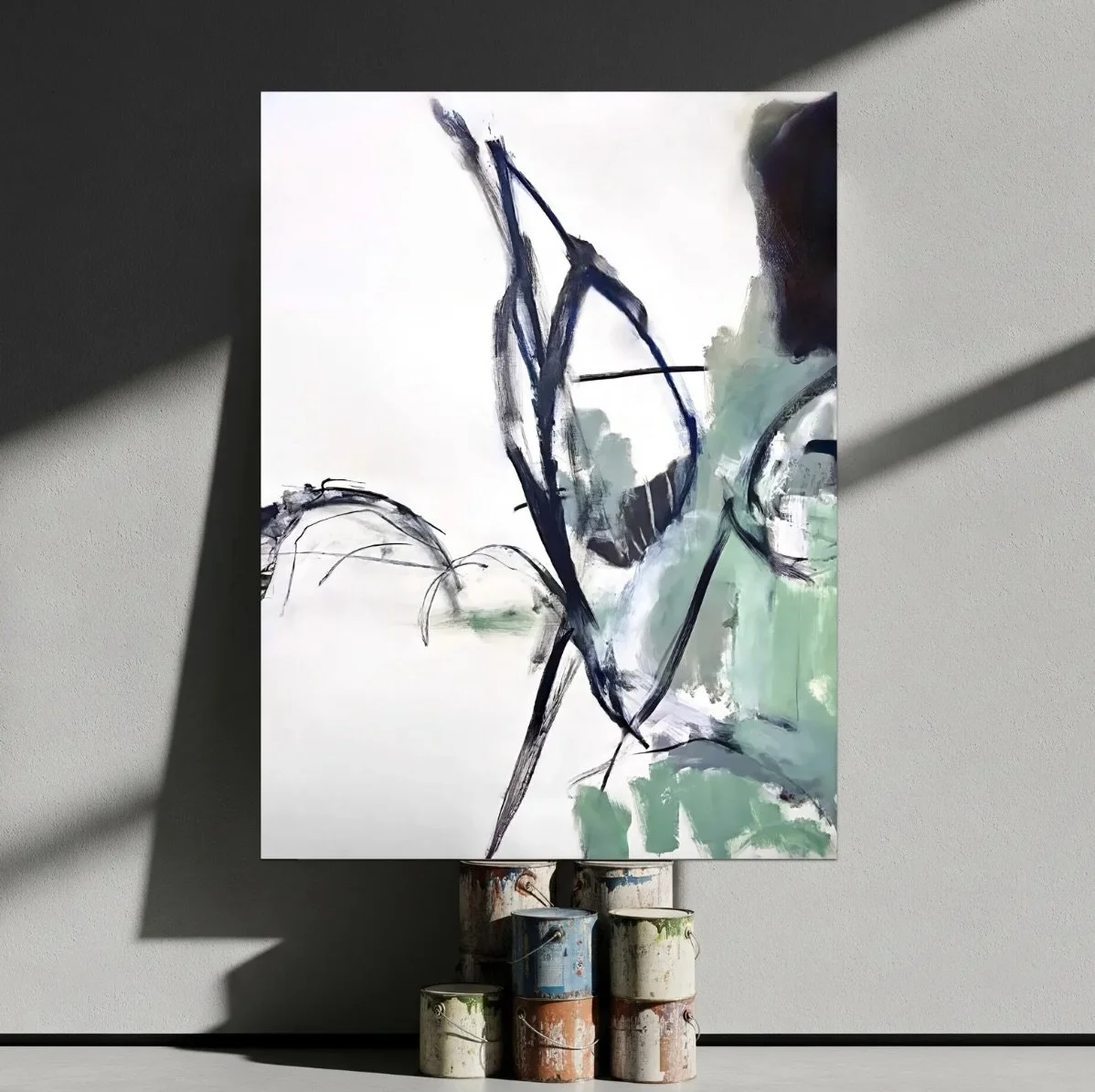 Abstract painting on canvas depicting bold black and blue strokes with hints of green, mounted on a wall with art supplies below.