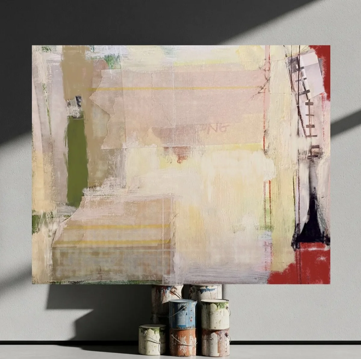 Abstract painting on a canvas, propped on paint cans, with geometric shapes and soft pastel colors, including beige, pink, green, and red, against a gray wall.