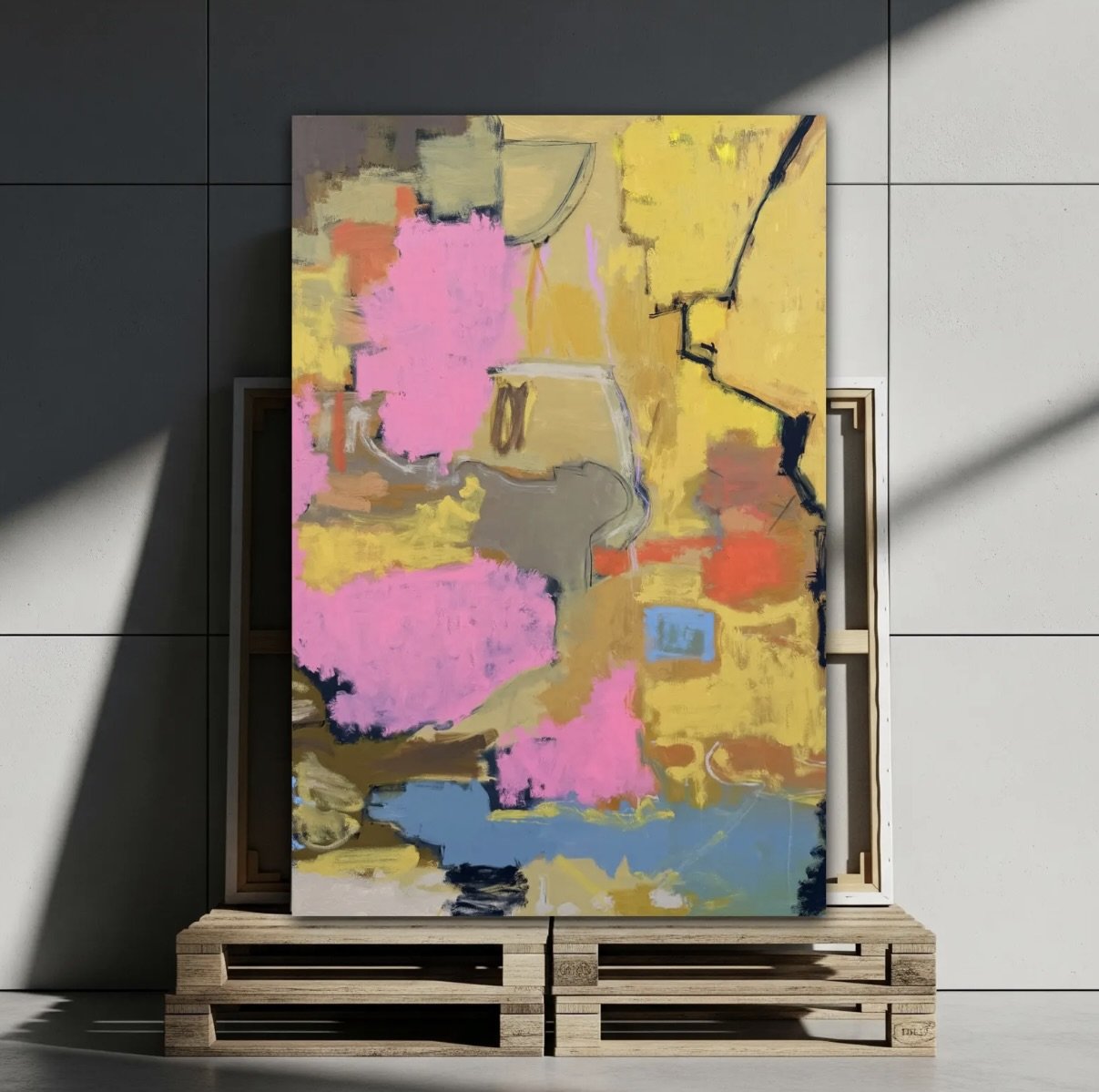 Abstract colorful painting with pink, yellow, orange, blue, and beige hues leaning against a wall on a wooden pallet.