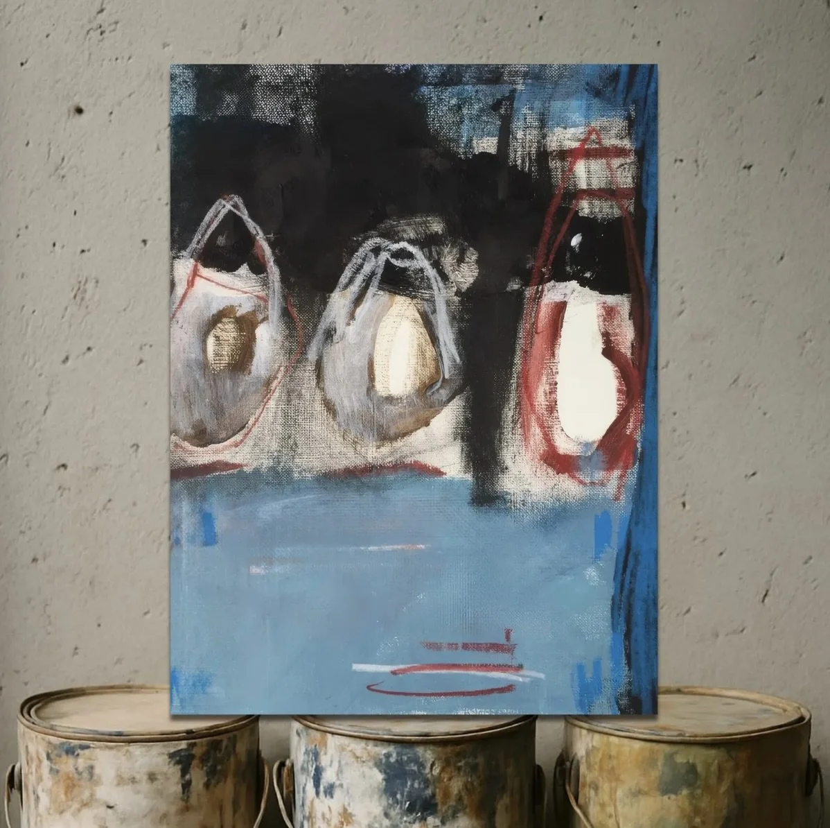 Abstract painting of three teapots with black, white, and red outlines, set on a blue background, leaning against a textured wall.