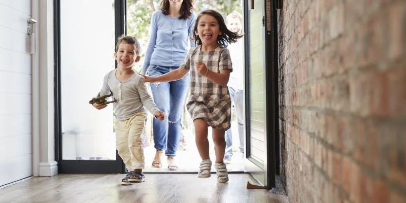Two children and an adult woman running out of a house through a door, smiling and enjoying themselves.