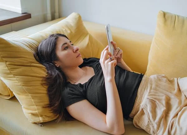 Young person lying on yellow couch using a smartphone.