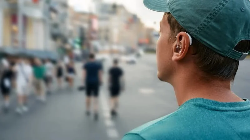 Close-up of a person man wearing a gray baseball cap and teal shirt and hearing aid
