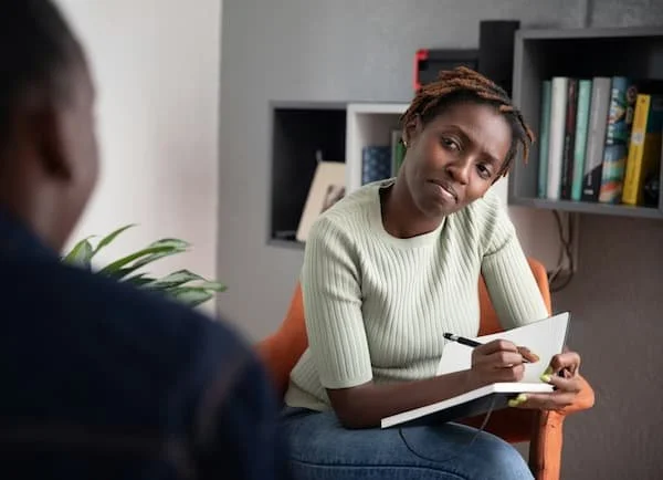 Person participating in a therapy session, holding a notepad and pen, with a skeptical or confused expression.