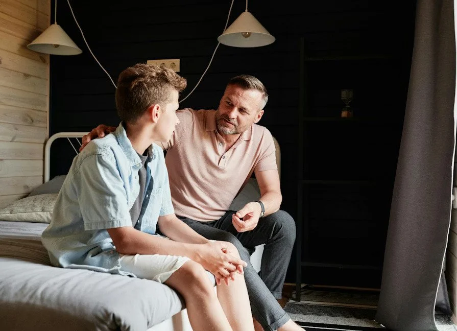 parent and teen sitting on bed talking