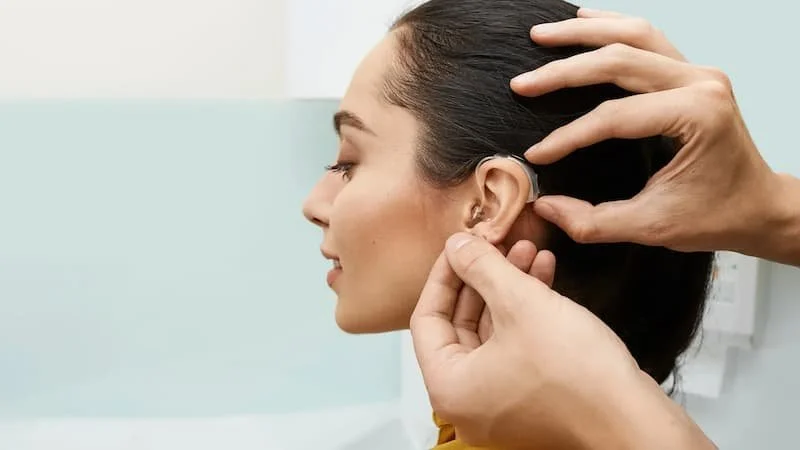 A person is getting a hearing aid inserted into their ear by a healthcare professional.