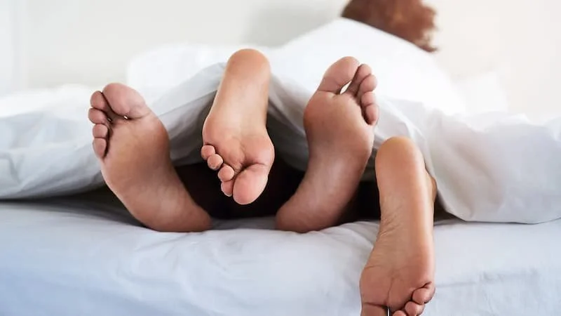 Multiple feet sticking out from under a white blanket on a bed.