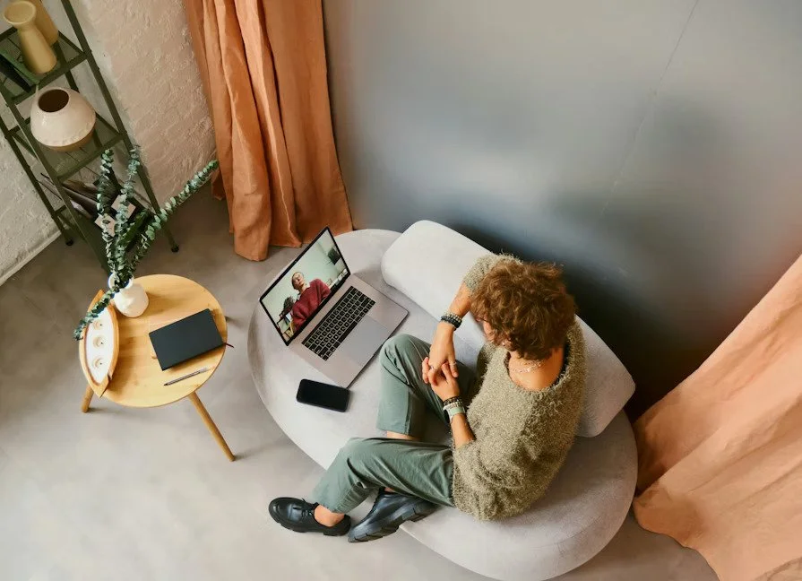 a person sitting on the couch with their hands crossed talking to therapist on video call