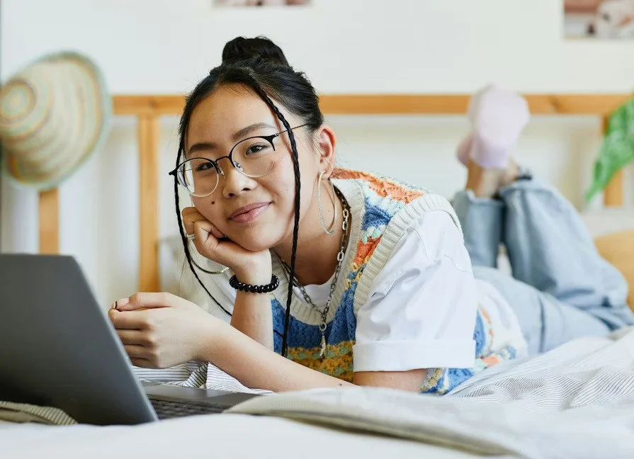 a teen laying comfortably on bed with laptop, slightly smiling