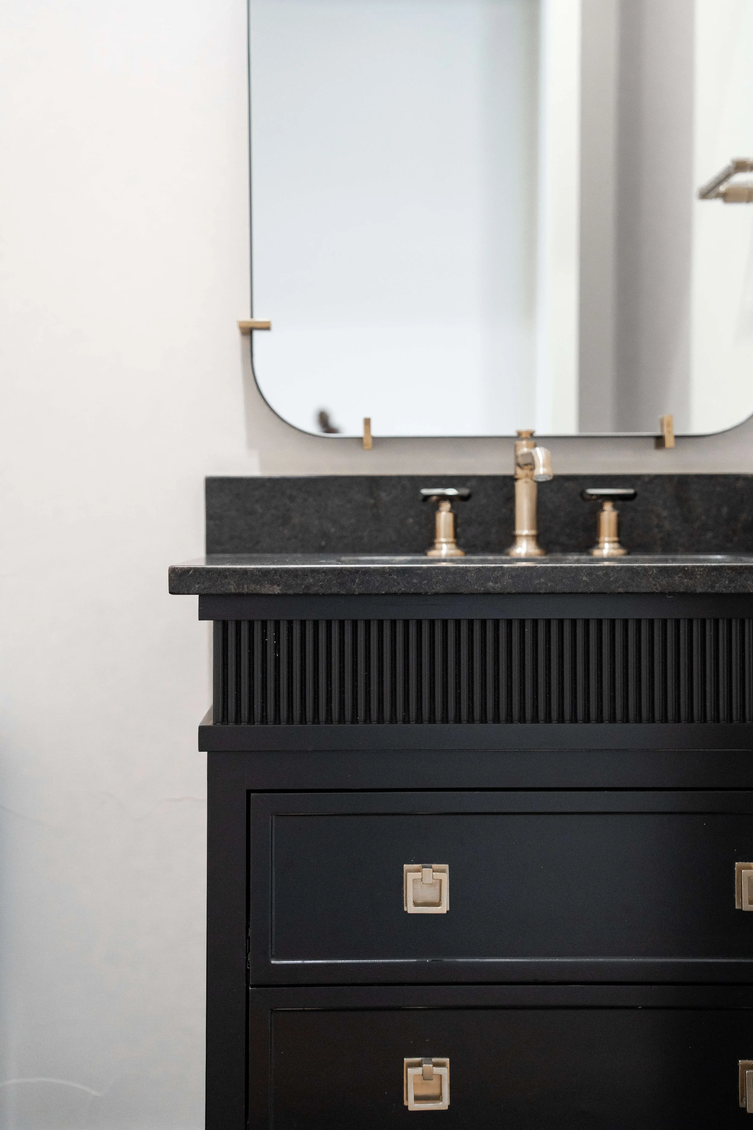Close-up of a black bathroom vanity with a black countertop, gold hardware, and a black-framed mirror mounted above it.