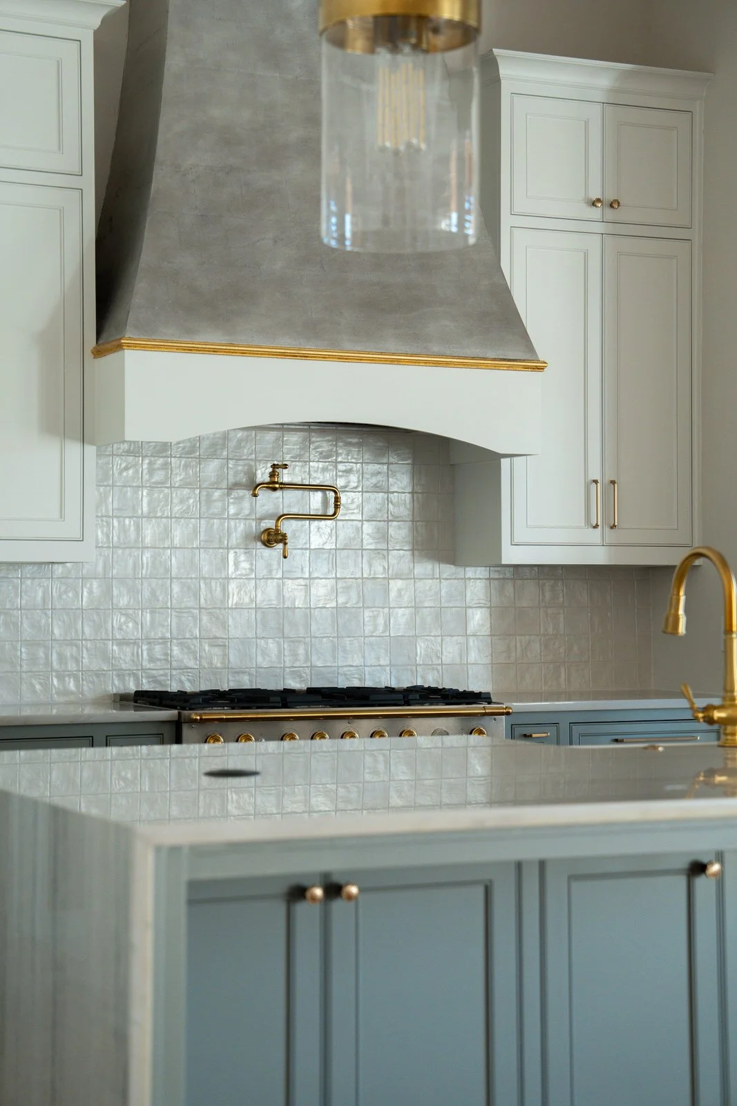 Modern kitchen with white cabinetry, gold hardware, a gas stove, tiled backsplash, and a gold faucet.