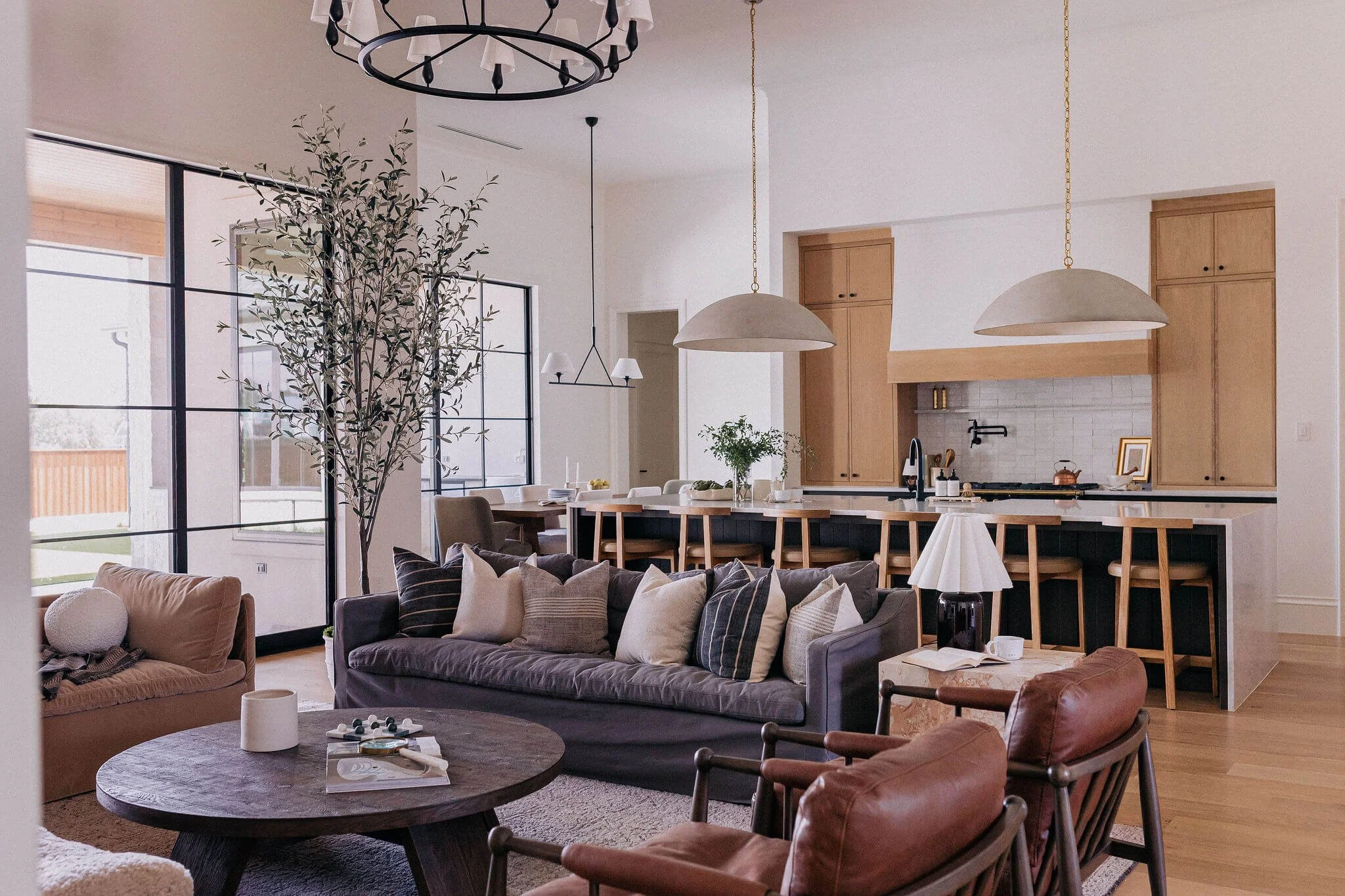 Keller, Texas open-concept living room and kitchen with a large sectional sofa, armchairs, a round coffee table, bar stools, and modern lighting fixtures.