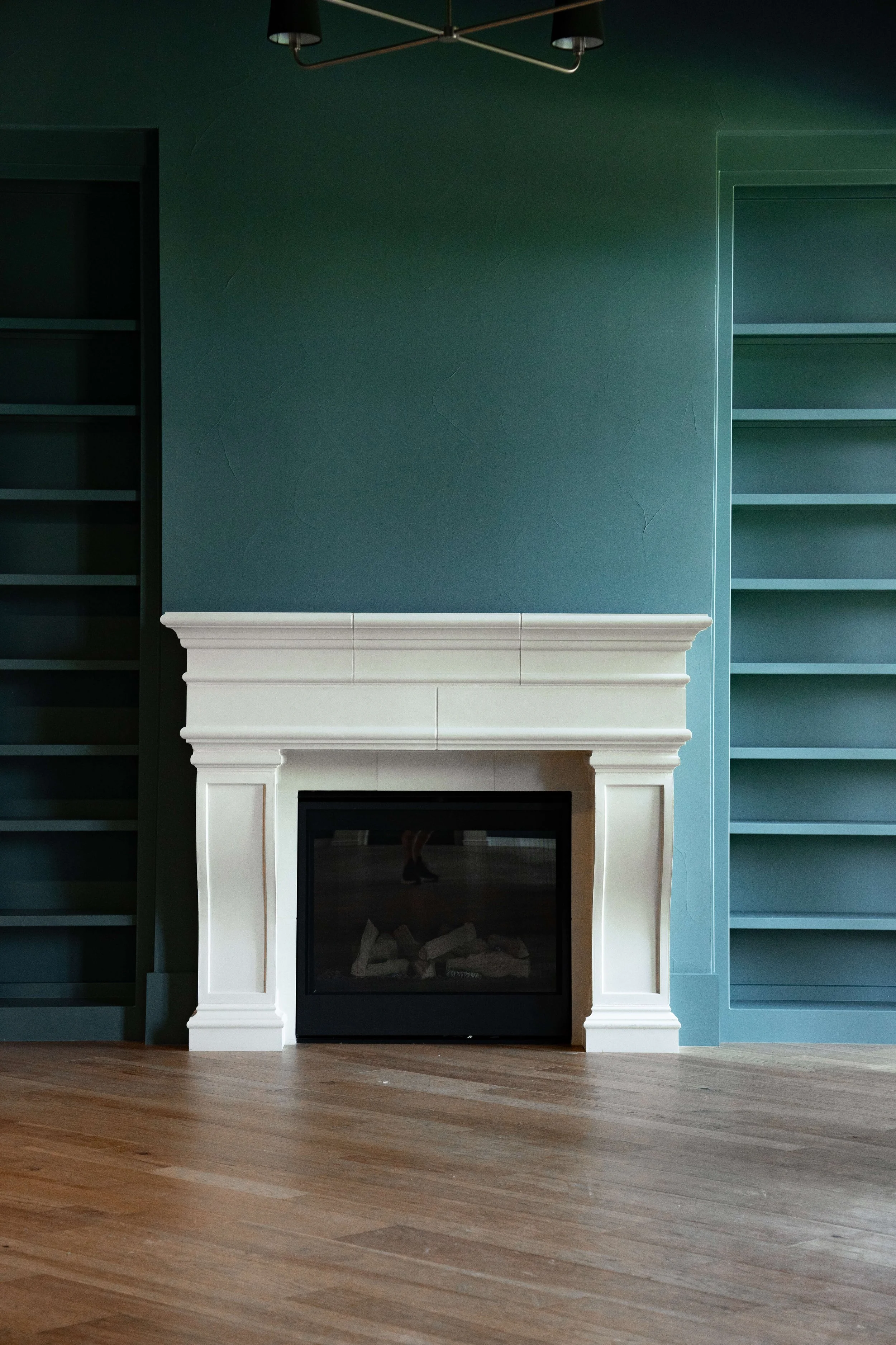 Grand living room with teal walls, a white fireplace, and built-in teal bookshelves on each side.