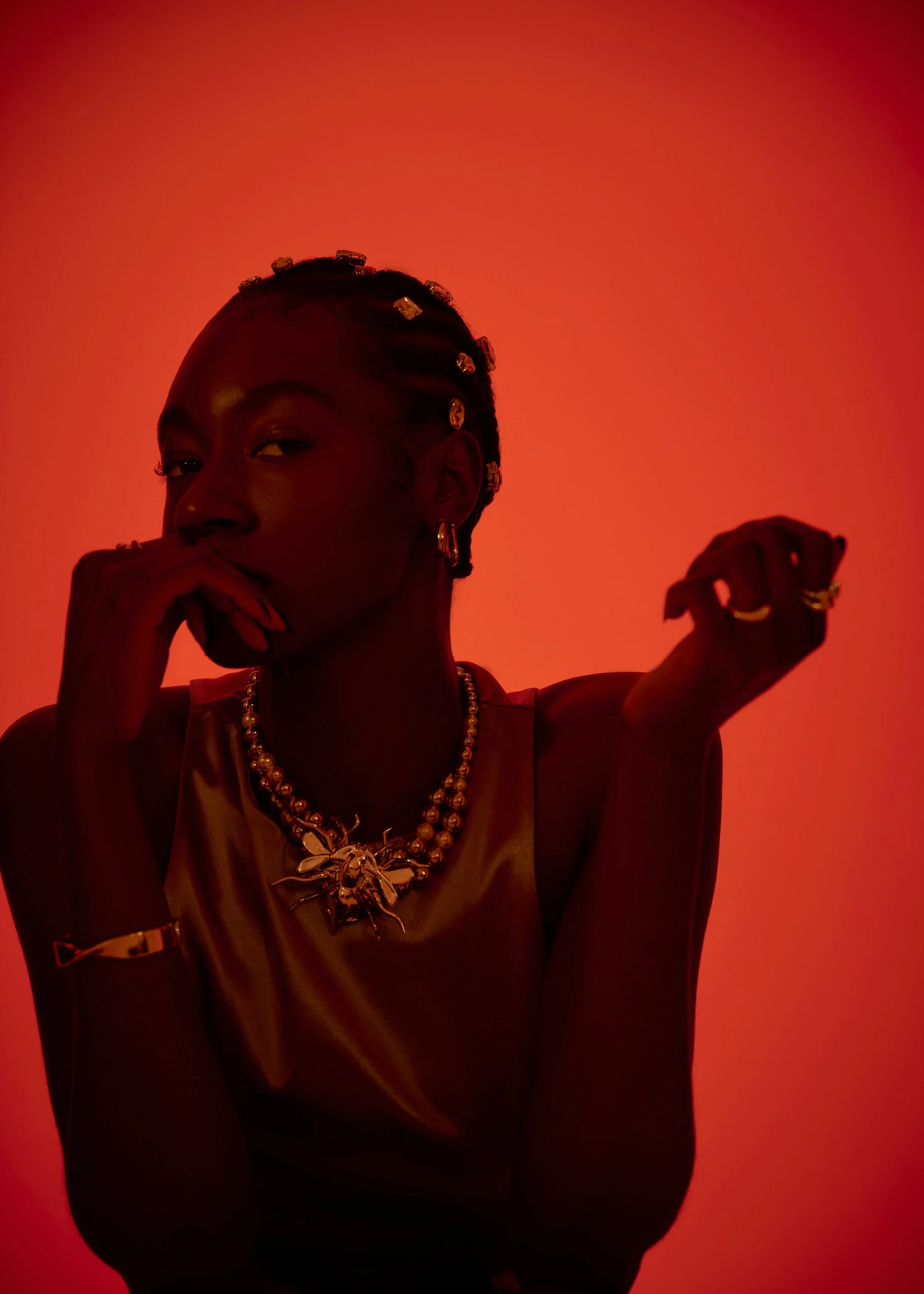Musician Ella-Simone adorned with silver accessories wearing a satin top, posed against a red background. Music album cover.