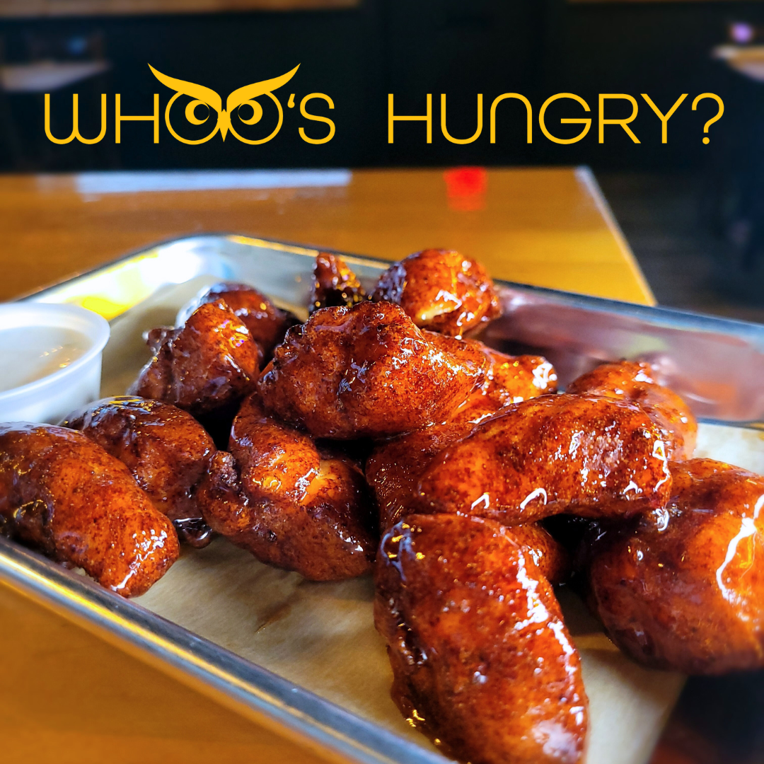Tray of glazed fried chicken wings with a small cup of dipping sauce on a wooden table.