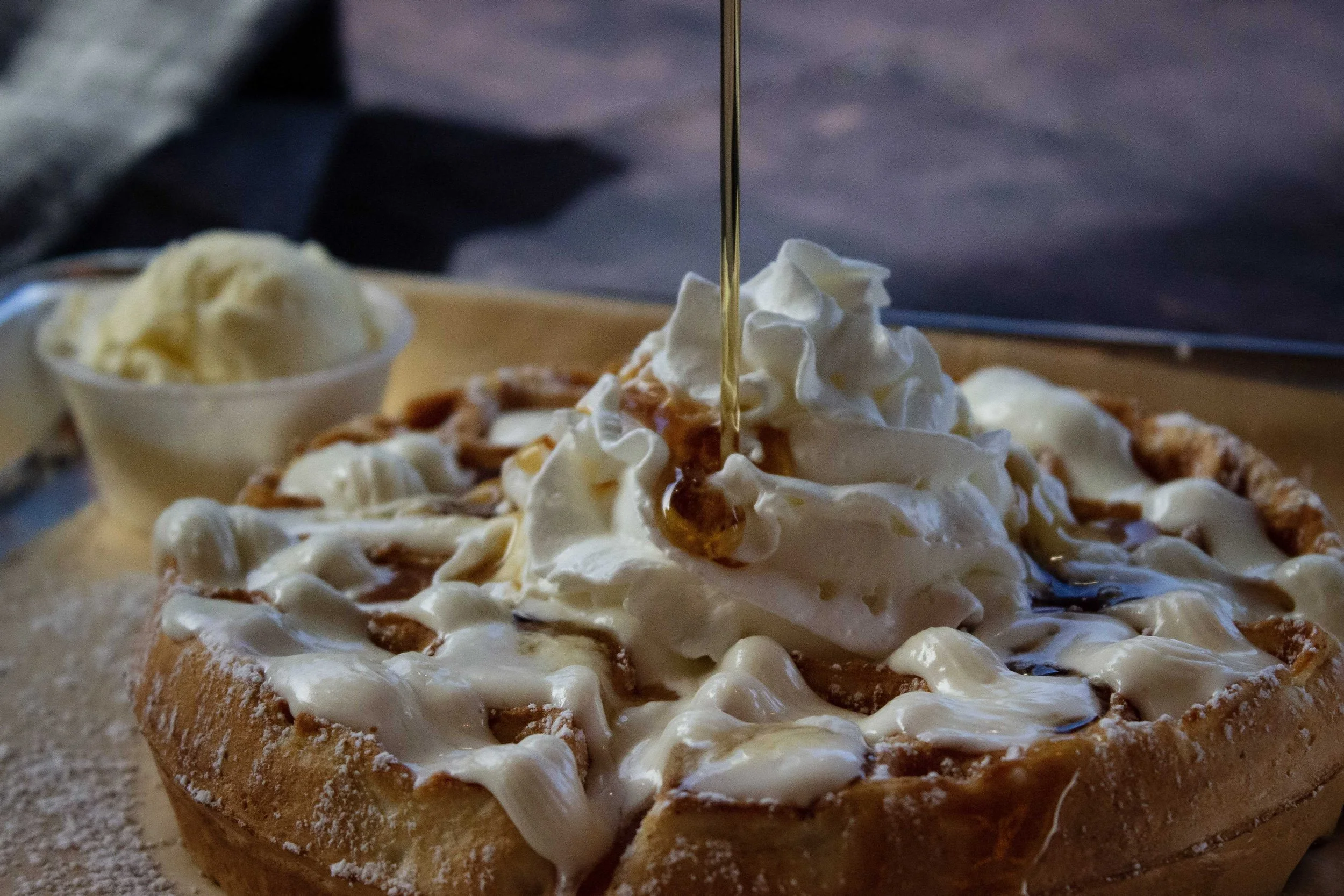 A dessert pizza topped with whipped cream and caramel syrup, with a side of vanilla ice cream in a small bowl.