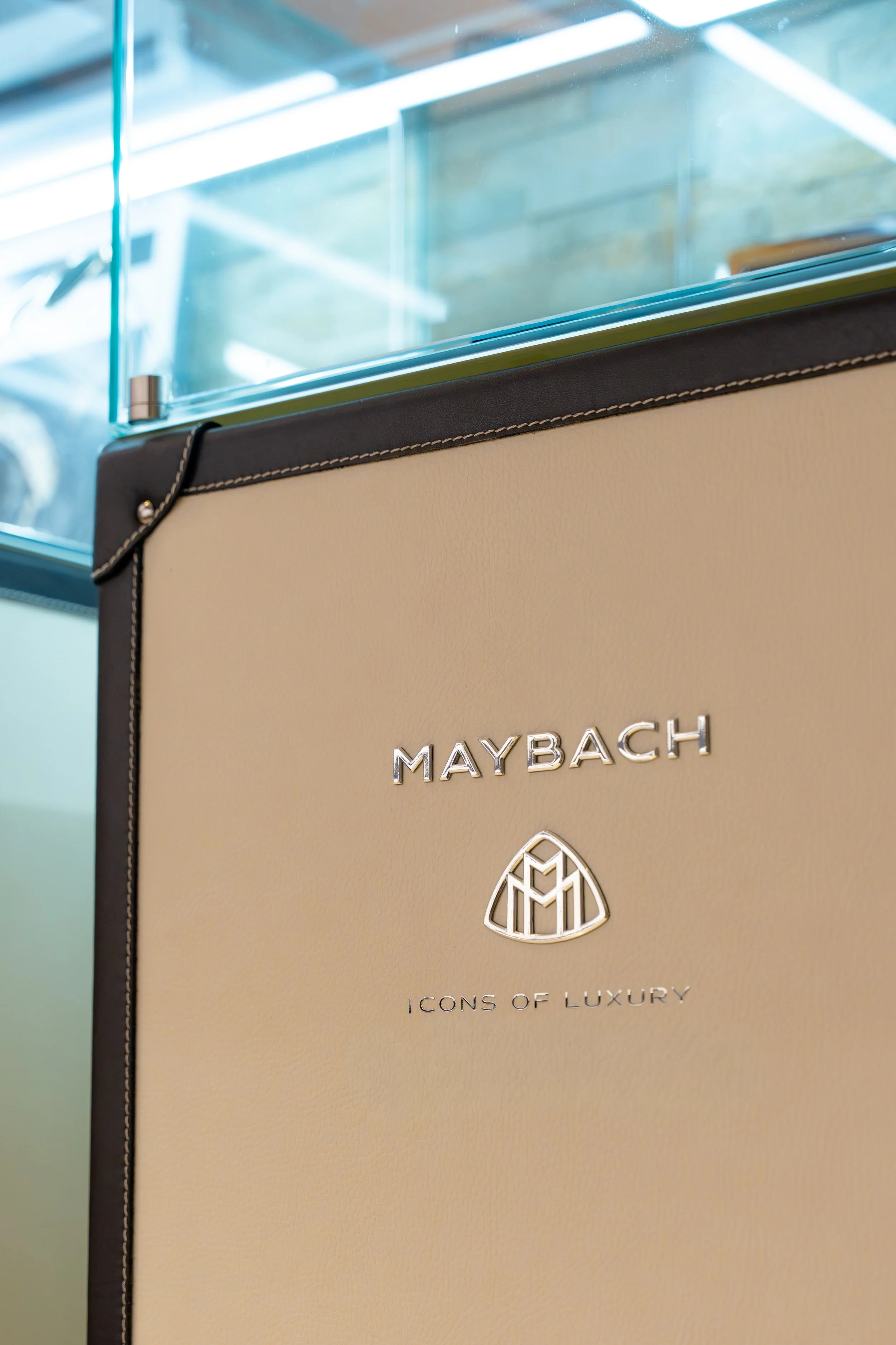 Nahaufnahme eines beige-farbenen Luxusprodukts mit silbernen Markenlogos, das die Marke Maybach repräsentiert, mit schwarzem Rand und weißen Nähten.
