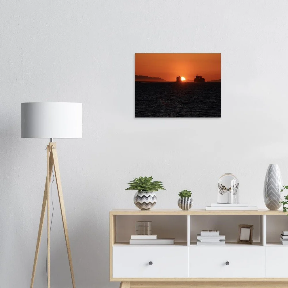 A living room with a wall-mounted sunset photo, a wooden floor lamp, and a white shelf with decorative plants, books, and ornaments.