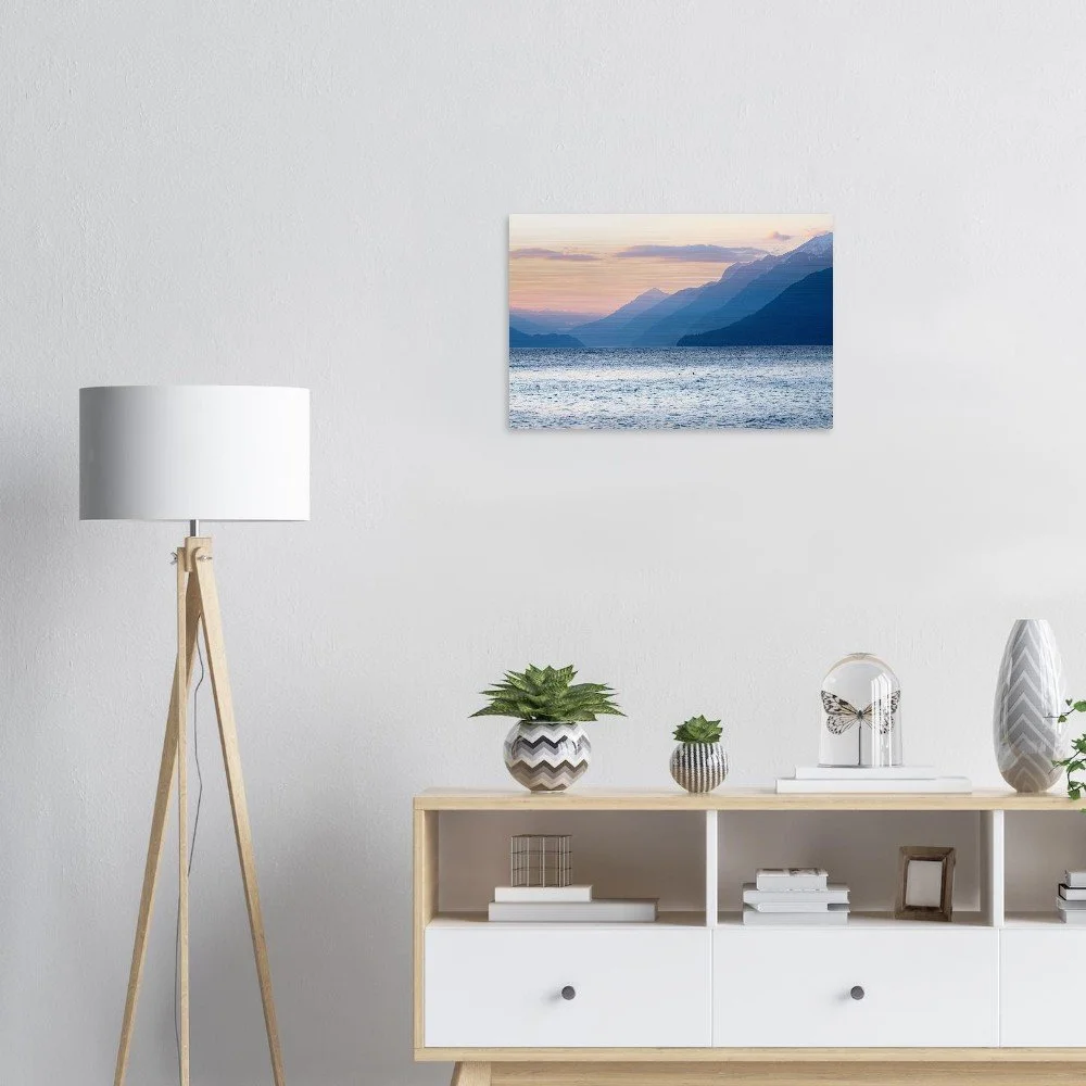 Living room with a mountain and lake landscape painting on the white wall, a white floor lamp with wooden legs, and a light wood TV stand decorated with books, plants, and decorative items.