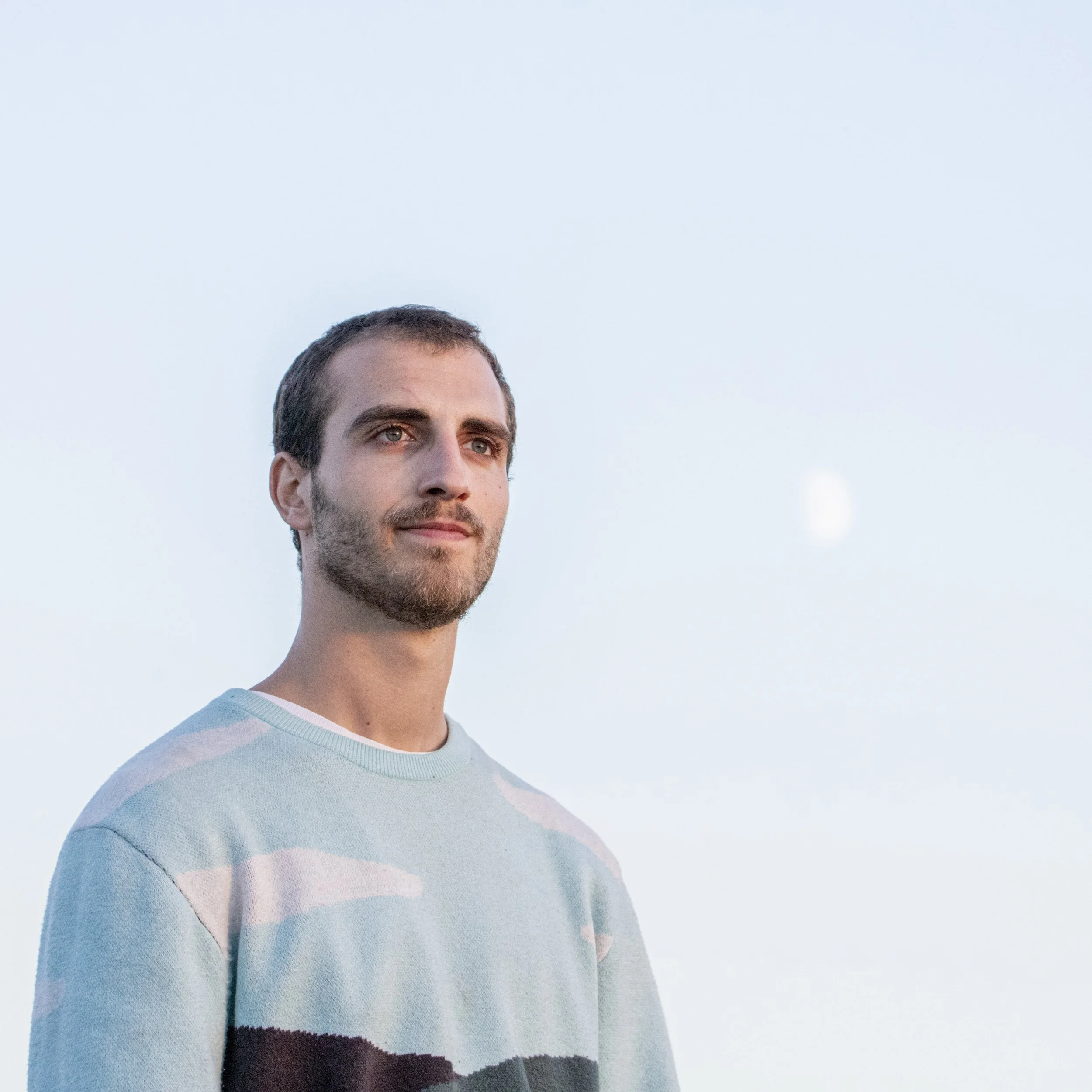 Paul Rophe, with short dark hair and a beard, standing outdoors against a clear sky, with the moon visible in the background.