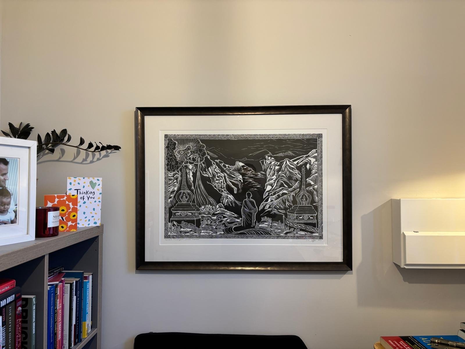 Intérieur d'une pièce avec un mur en briques de style carreaux de parquet, un tableau noir et blanc dans un cadre noir accroché au mur, une sculpture organique en bois ou en résine blanche fixe un objet en bas à gauche, un radiateur rouge en dessous du tableau, une partie d'un animal avec un pelage marron clair et blanc visible à droite.