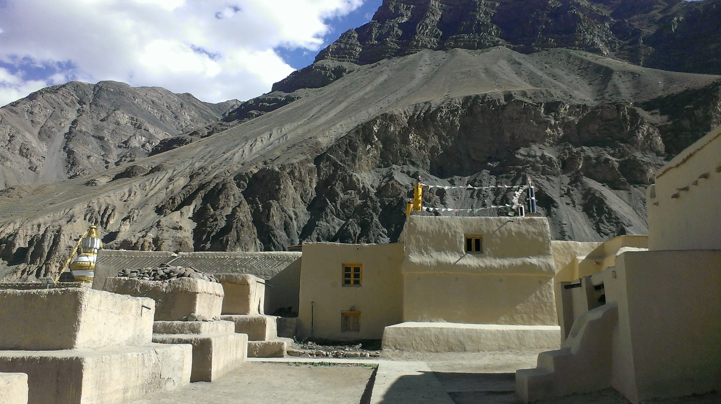 Village avec maisons en pierre blanche, entouré de montagnes rocheuses.