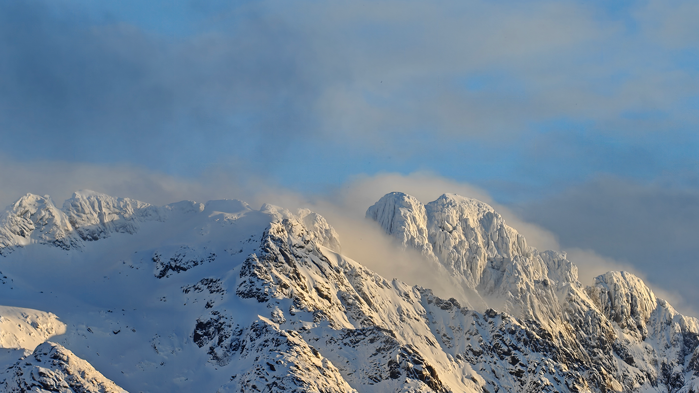 Montagnes enneigées sous un ciel partiellement nuageux.