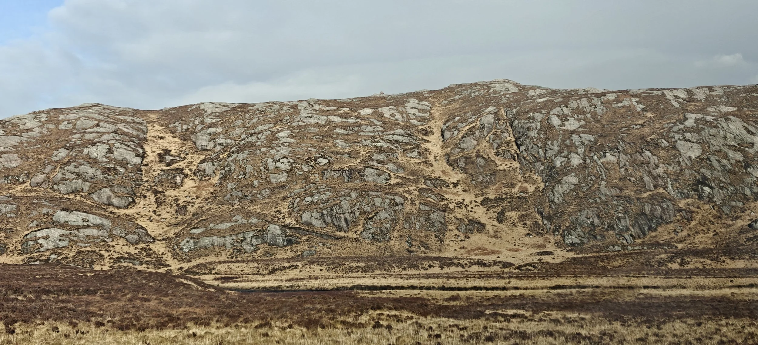 Un paysage de collines rocheuses avec de l'herbe brune et un ciel nuageux.