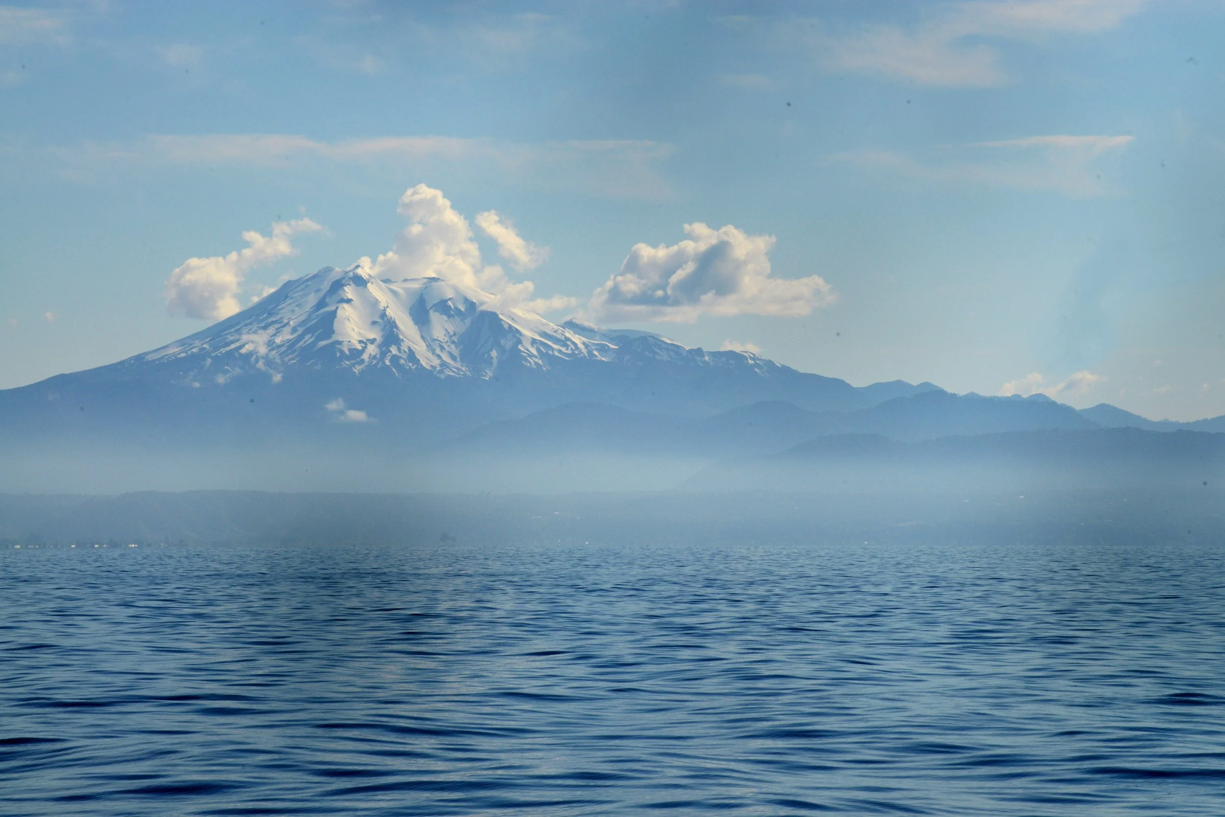 Montagne enneigée avec un lac en premier plan, ciel bleu avec quelques nuages.