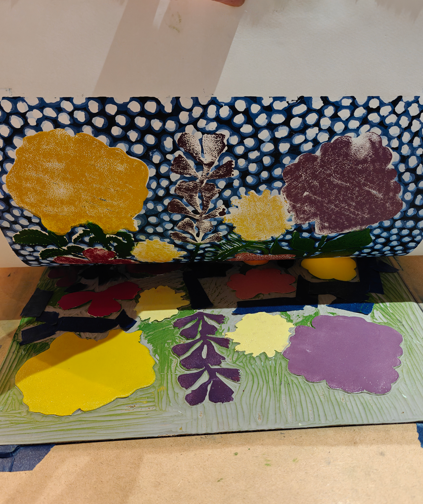 Deux vitrines avec des œuvres d'art en papier découpé représentant des fleurs et des feuilles colorées, placées sur une surface en bois.