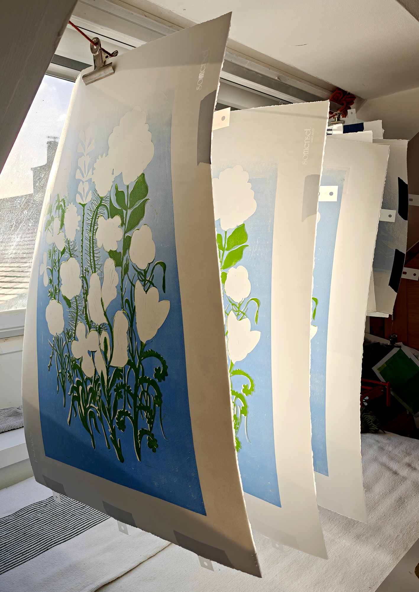 Affiches ou panneaux publicitaires avec une illustration florale de fleurs blanches et de feuilles vertes sur un fond bleu, suspendus à une corde à linge.