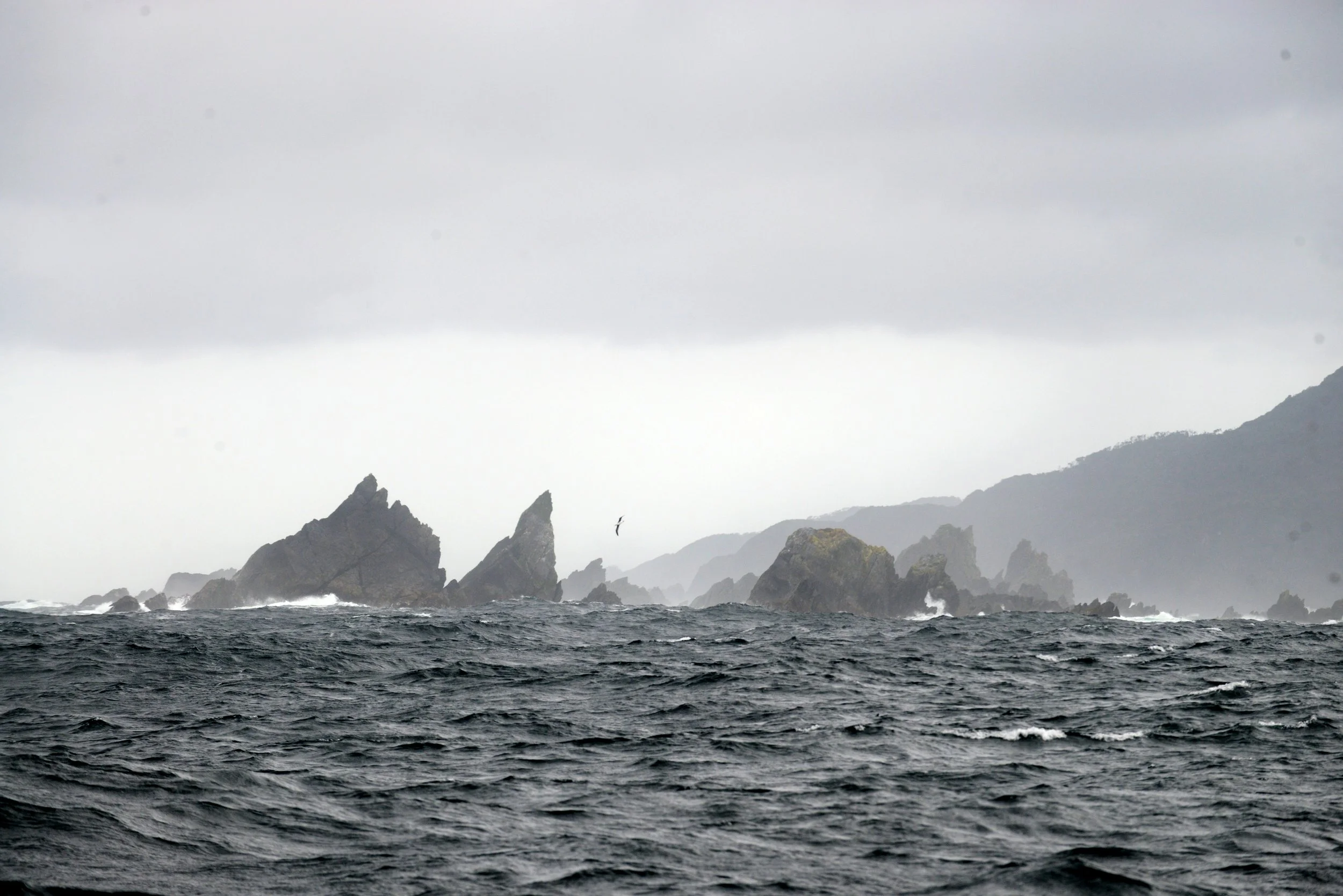 Mer agitée avec des rochers escarpés en arrière-plan sous un ciel nuageux