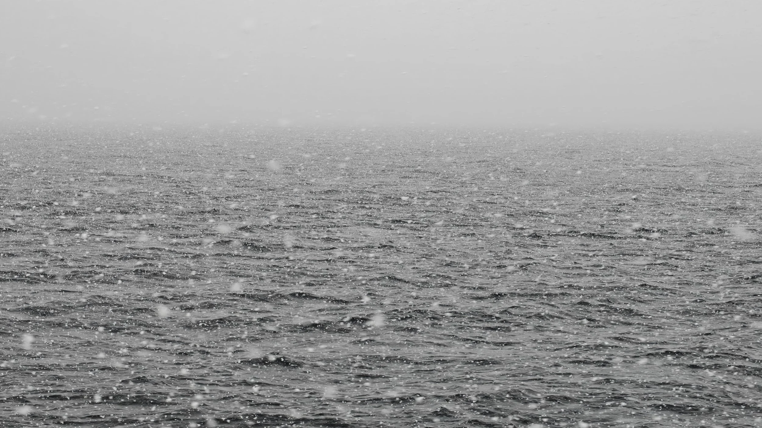 Vue de la mer sous une pluie battante, ciel gris et mer agitée.