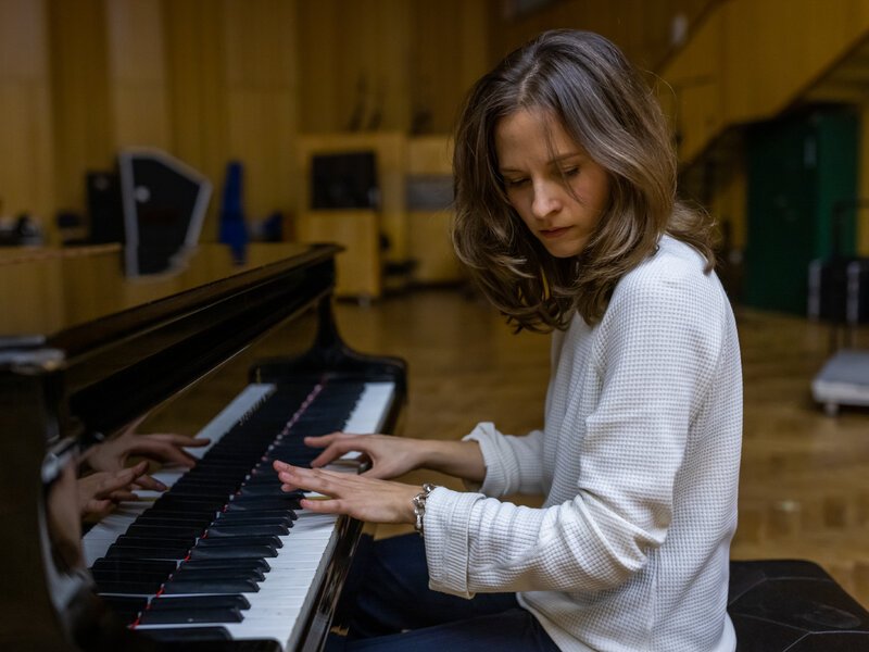 Une jeune femme joue du piano dans une salle de musique, concentrée sur ses mains sur le clavier.