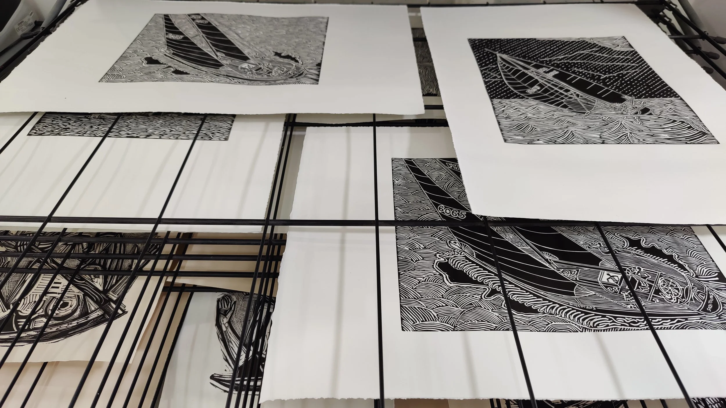 Impressions en noir et blanc de dessins de bateaux, placées sur un grille pour le séchage.